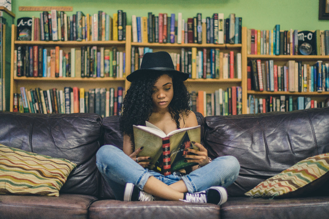 Girl in a cool hat sitting on a couch in a book shop reading