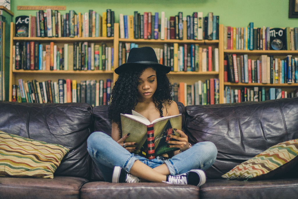 Girl in a cool hat sitting on a couch in a book shop reading