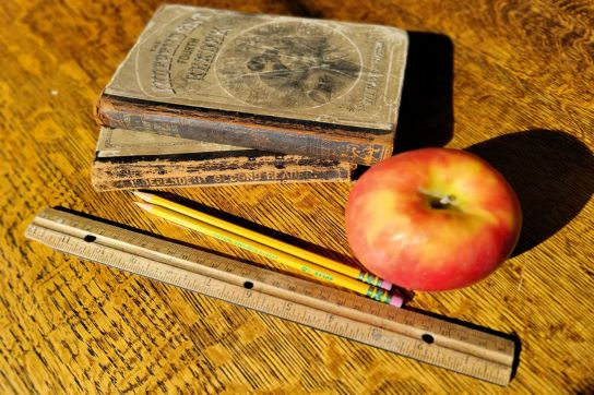 An apple next to a ruler, pencils, and old books