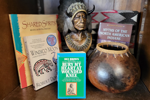 A statue of a man in a native american headdress next to old pottery and various books on Native American studies